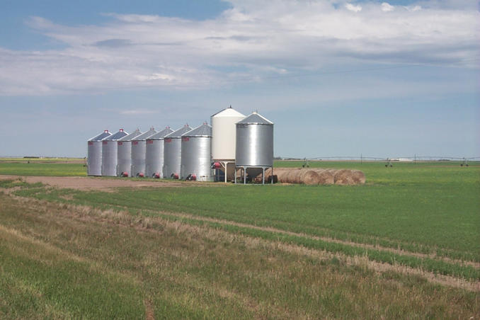Grain bins and hay bales with sprinkler system in background.