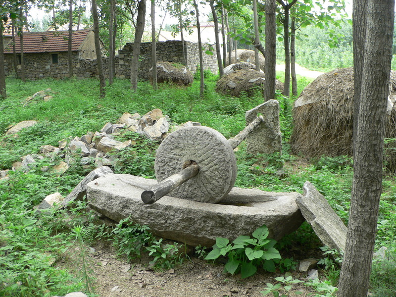 Millstone, with a stone house and wall in the background