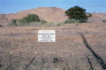 #1: The confluence is located 168 feet beyond this security fence - probably close to the oak tree on the right