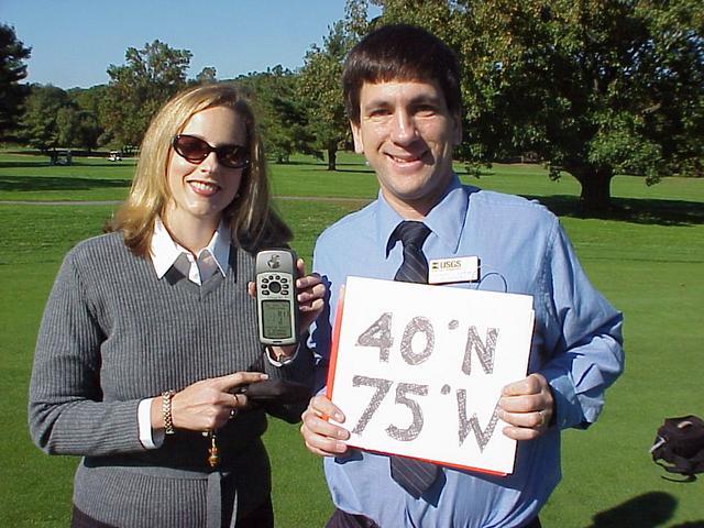 Geography educators Joseph Kerski and Mary Braccili holding GPS receiver and sign at the confluence.