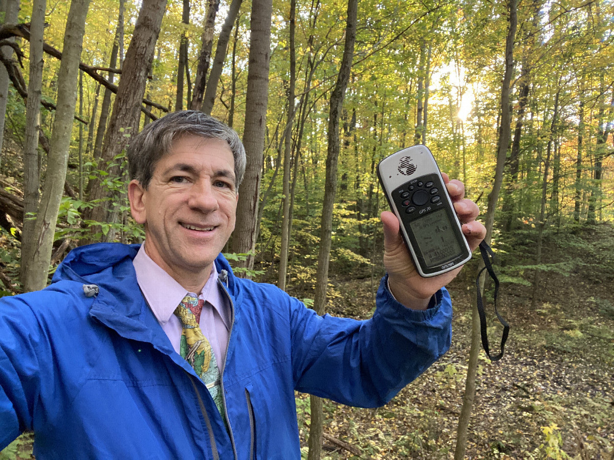 Joseph Kerski wearing map tie in the forest at the confluence point. 