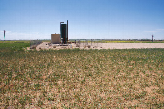 #1: AS The confluence point lies in a flat, grassy field, surrounded by businesses supporting the petroleum industry.  (This is also a view to the South, towards a nearby petroleum processing facility.)