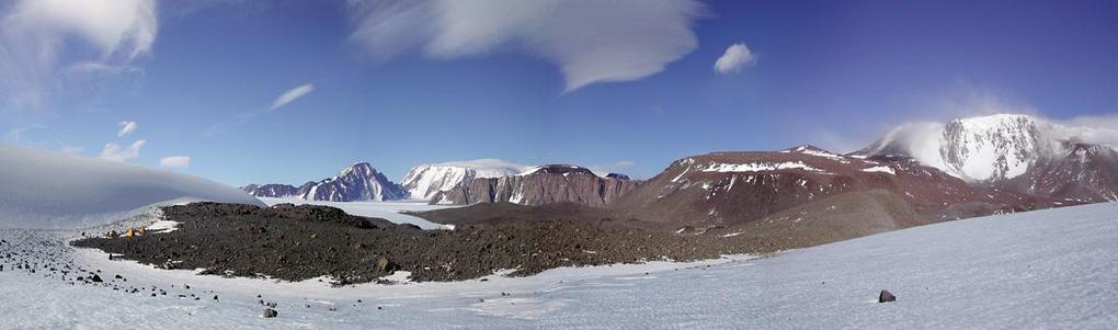 A panoramic view of the area.  The confluence is located at center-right, on the red-brown hillside in front of the misty escarpment.