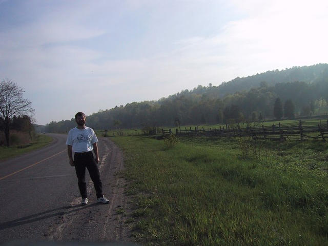 Markus with the confluence site in the woods in the middle background