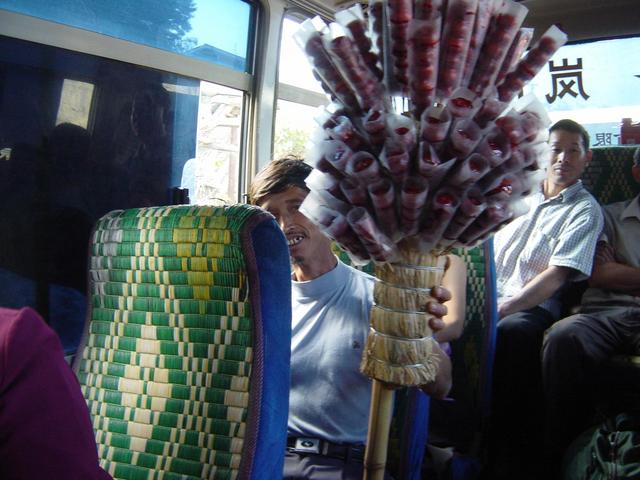 Bus passenger with pole of candied crab apples on bamboo skewers
