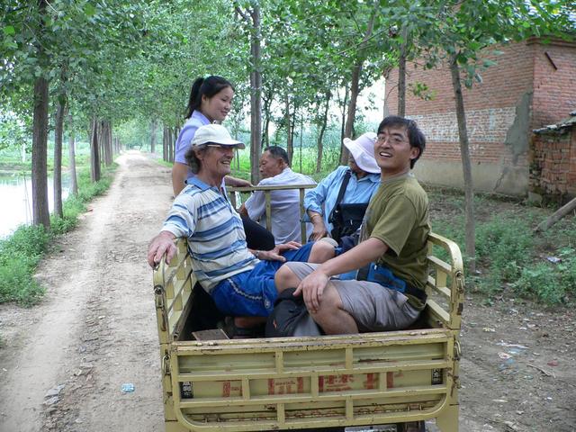 Dong Lili standing, and Jim, Nur and Xiao Xu sitting on tiny wooden stools in back of truck.