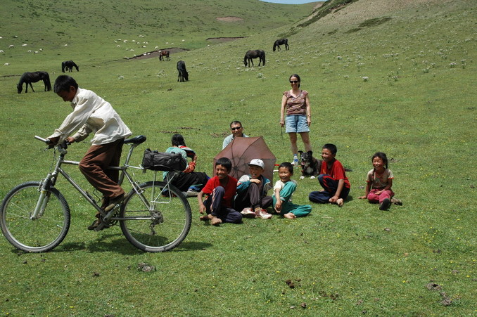 The waiting party and the Yak herders with one of them trying out the mountain bike