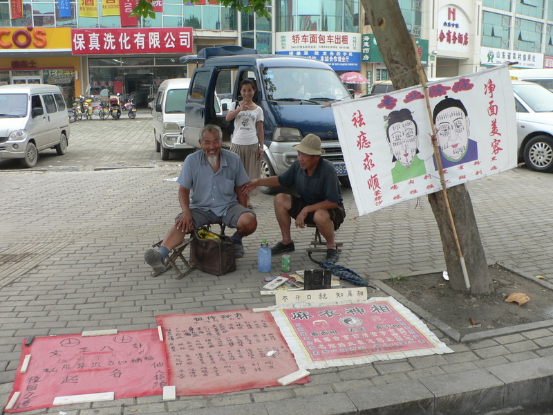 Ah Feng standing behind a couple of roadside fortune-tellers in Hézé