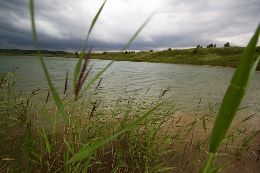 The confluence point lies in this large pond, 23m away.  (This is also a view to the West; note the approaching thunderstorm.)