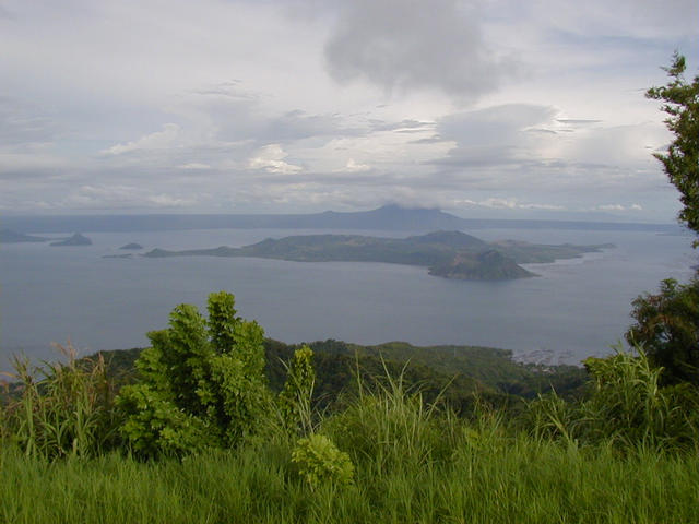 The confluence sits on the backside of Volcano Island (center of photo) in Taal Lake. View is SSE from the town of Tagatay on the northern rim of the pre-historic Taal Volcano. The Southern rim and Mt. Maculot (shrouded in clouds) are in the background.