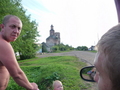 #7: Pavel grimacing at Evgeny explaining the confluence concept to him. View of hamlet, dilapidated cathedral and our white jeep Niva in the background.