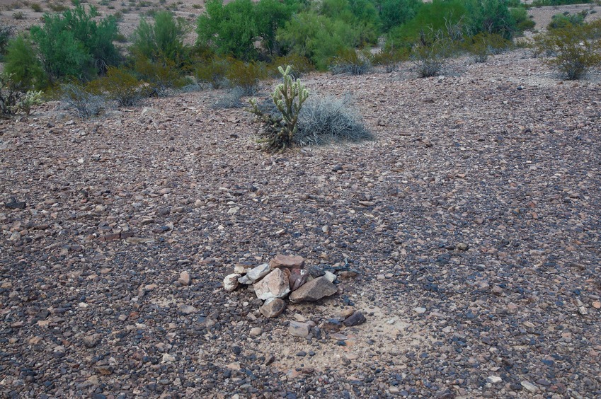 The confluence point lies in a stony, sparsely-vegetated desert