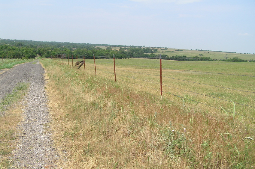View to the east from the crest of the hill 500 meters east of the confluence, looking west.  The confluence lies in the trees at the left end of the photograph where the road leads.