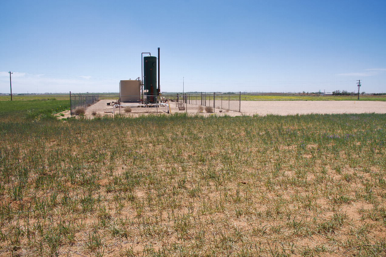 AS The confluence point lies in a flat, grassy field, surrounded by businesses supporting the petroleum industry.  (This is also a view to the South, towards a nearby petroleum processing facility.)