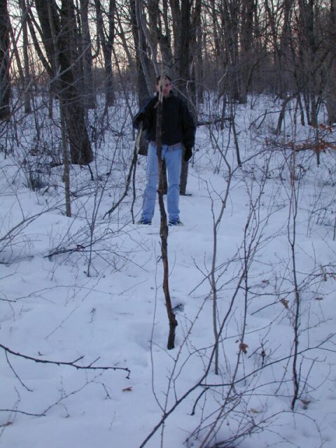 Tom stands about ten feet back from the big stick upright in the snow marking our confluence estimate